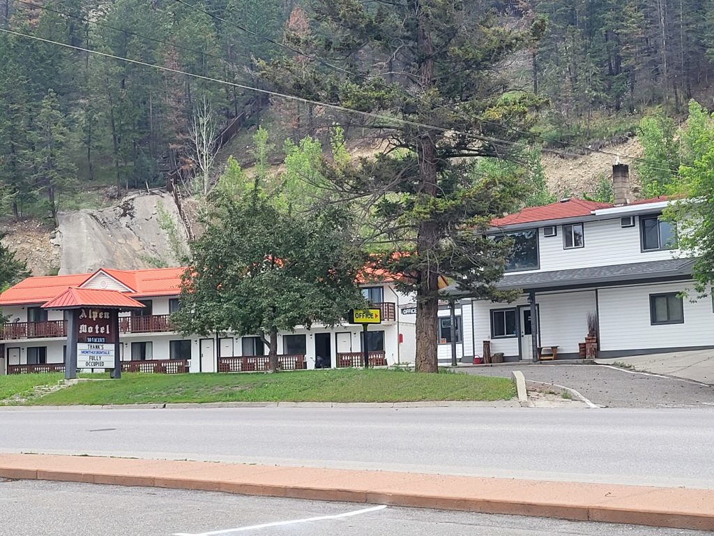 Outside street view of Alpen Motel with an empty street and views of nearby trees.