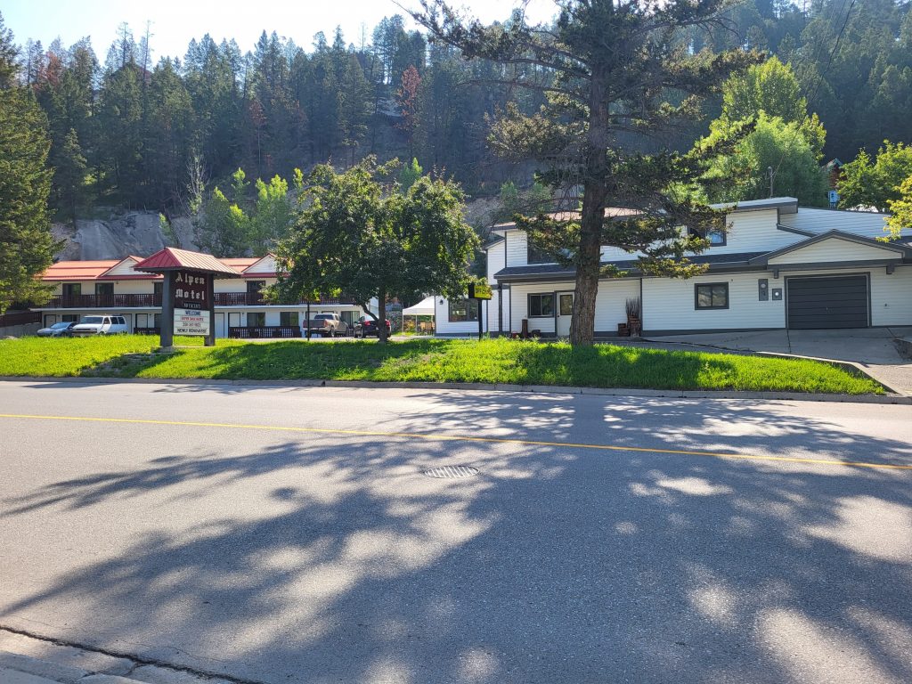 Outside view of a motel with trees casting shadows across the street in the sunny weather.