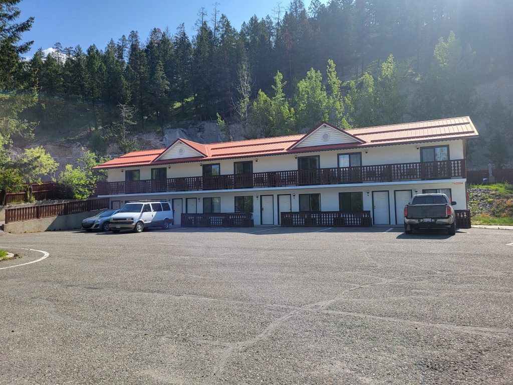 Alpen Motel outside view with spacious parking lot against the backdrop of mountain forest.