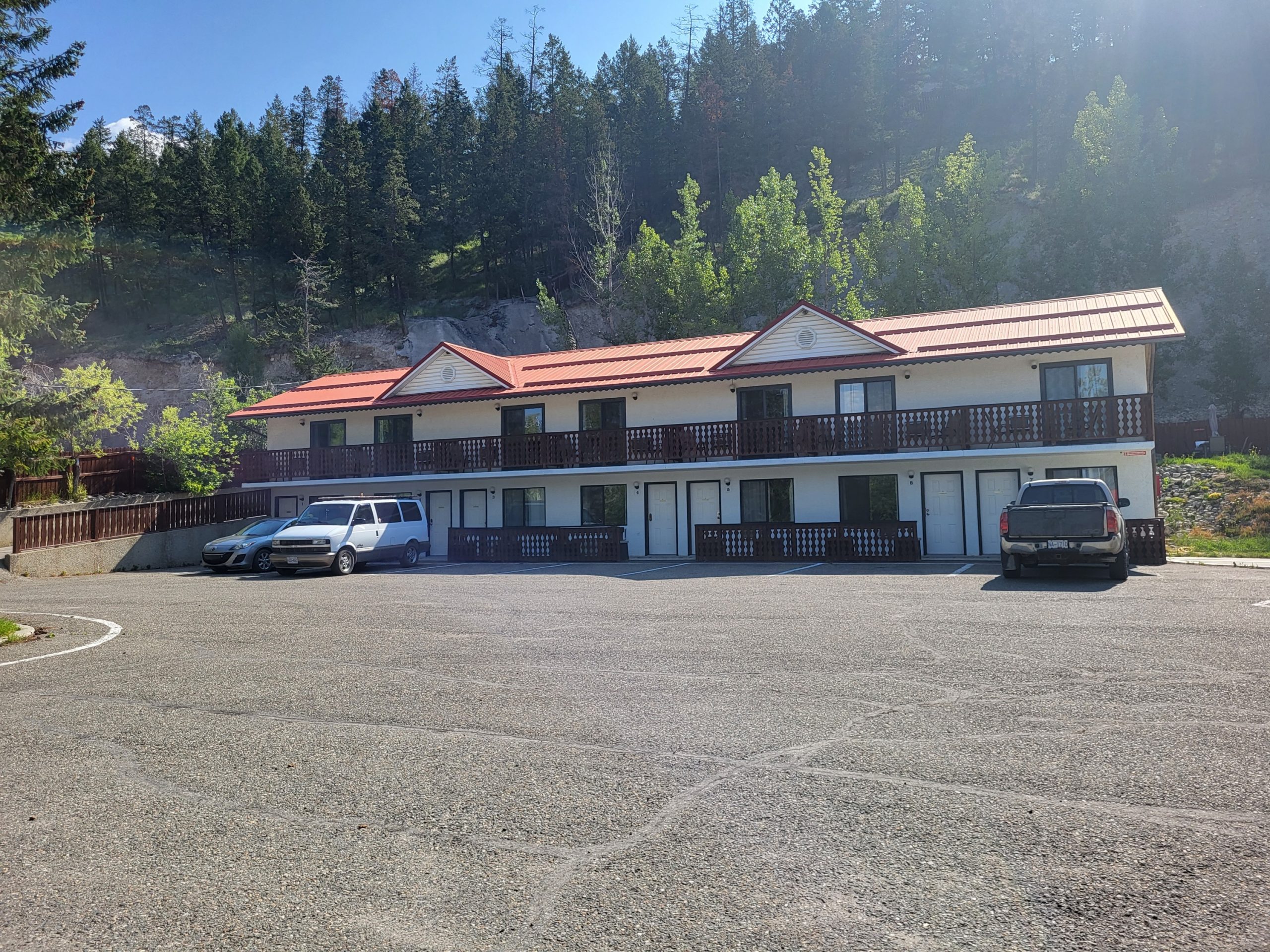Alpen Motel outside view with spacious parking lot against the backdrop of mountain forest.