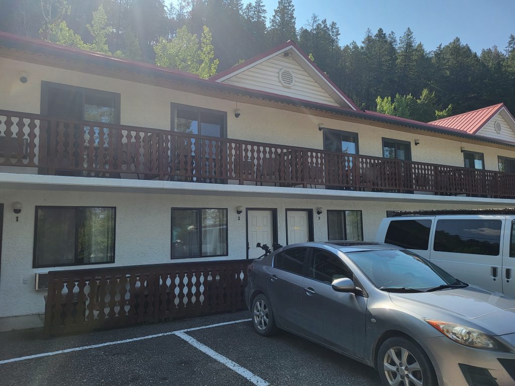A car parked in front of a motel with a balcony and rows of doors to the rooms.