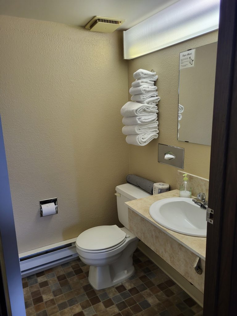 A clean motel bathroom showing a toilet and a rack of white linen towels.