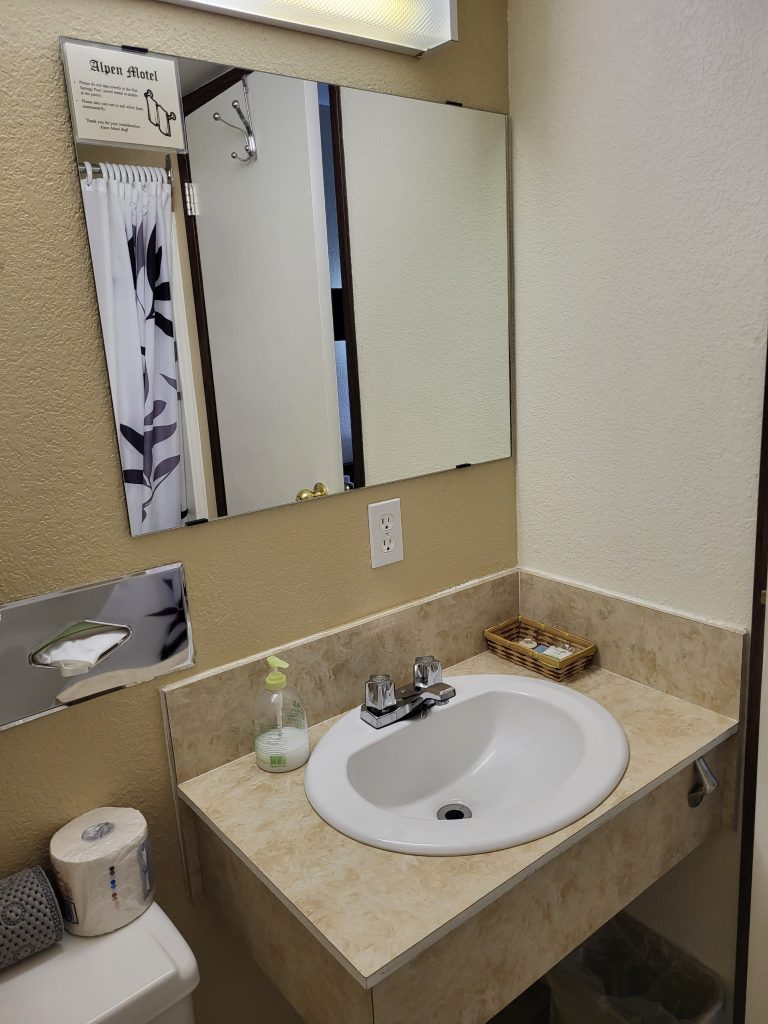 A clean motel bathroom with white sink and a square mirror.