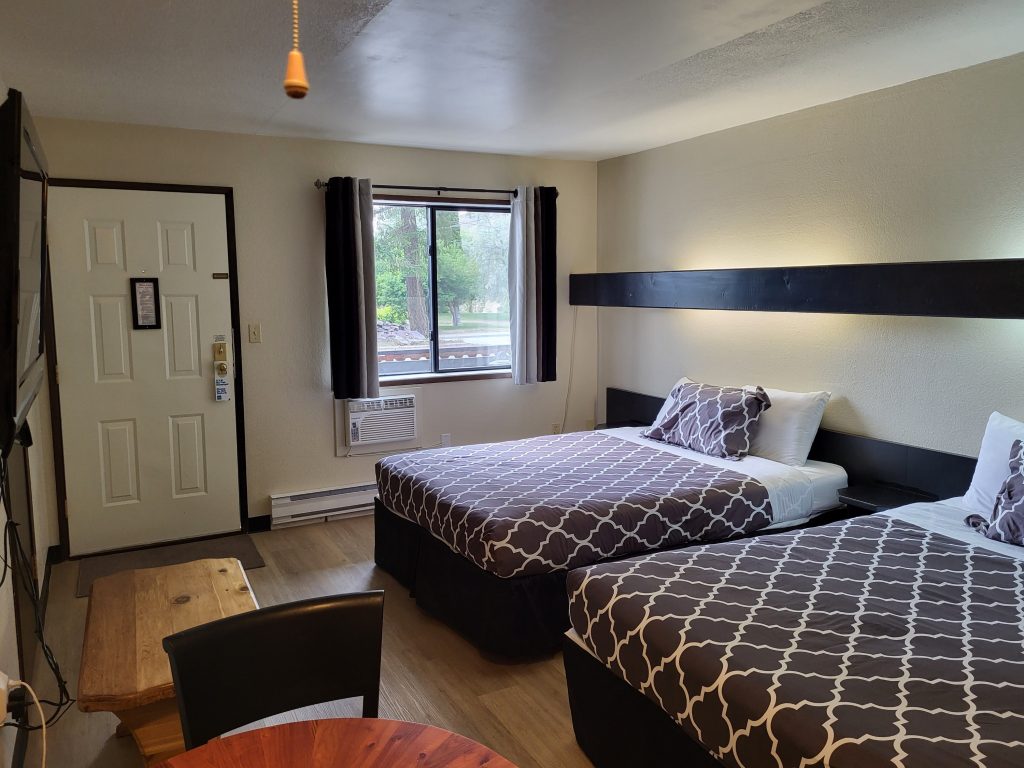 A double twin queen bed room of a motel with a window looking out onto the balcony.